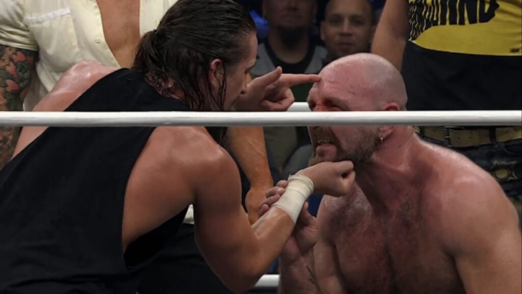 Jay White holds Jon Moxley’s chin and points at his forehead during The Bang Bang Gang and The Dogs’ attack on AEW Dynamite, October 21, 2026.